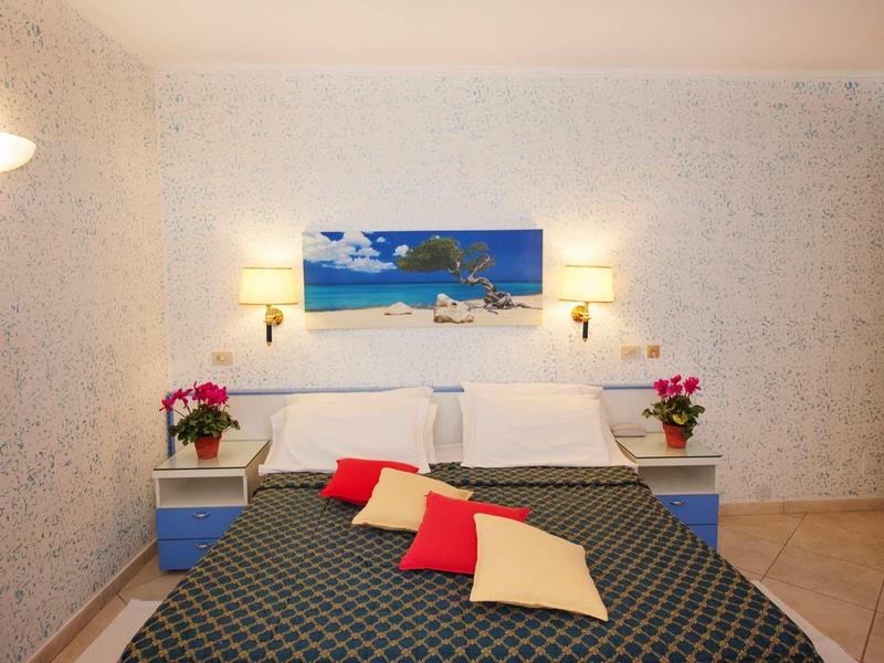 Gezellige hotelkamer met tweepersoonsbed, kleurrijke kussens en een maritiem schilderij aan de muur.
