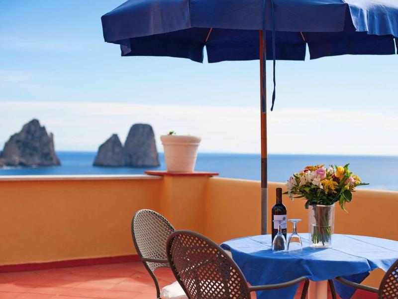 Terras met blauwe tafel, stoelen, parasol en zeezicht met rotsen op de achtergrond