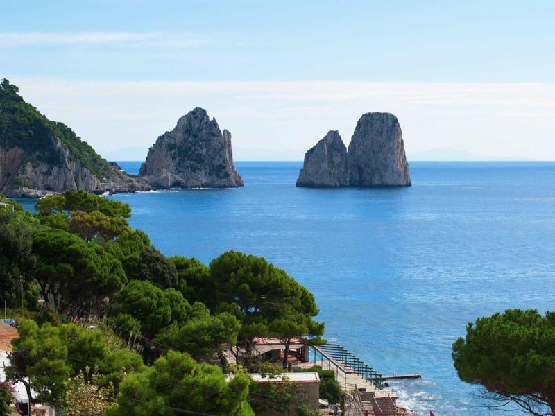 Kustlijn met groen begroeide heuvels en rotsen in blauwe zee onder heldere lucht.