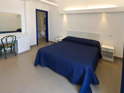 Modernes Schlafzimmer mit blau gedecktem Doppelbett, weißem Tisch, Stuhl und großem Spiegel.