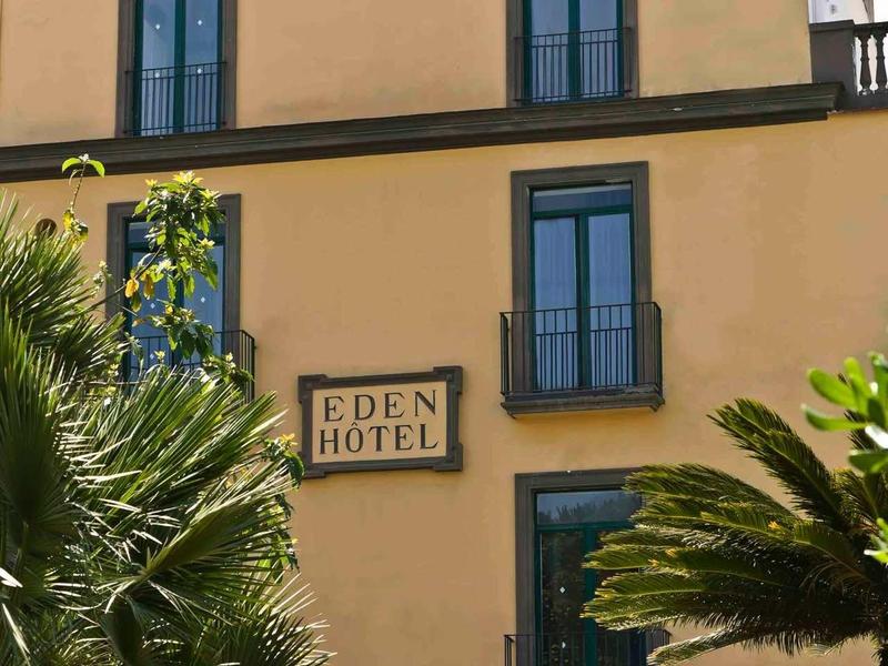 Mehrstöckiges, beiges Hotelgebäude mit blauen Fenstern, umgeben von grünen Palmen.