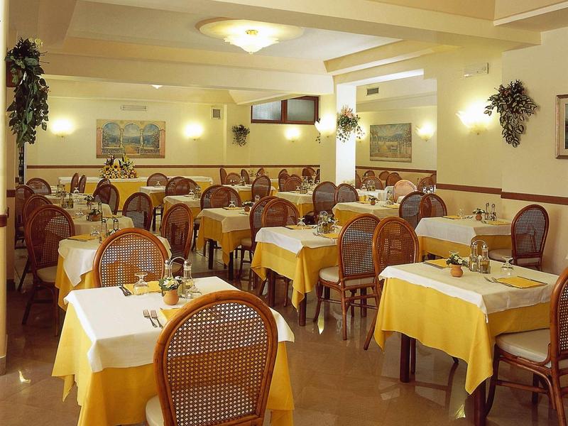 Gemütlicher Speisesaal mit Holzmöbeln, gelben Tischdecken und gedeckten Tischen.