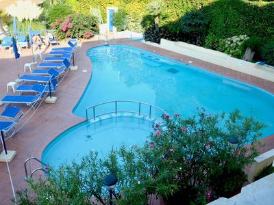 Außenpool mit Liegestühlen und üppiger Bepflanzung in einem Hotelgarten.