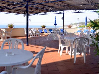 Offene Terrasse mit weißen Kunststoffstühlen und Tischen mit Blick auf das Meer.