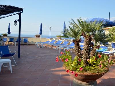 Terrasse mit Blumendekoration, Liegestühlen und Blick auf das Meer an einem sonnigen Tag.