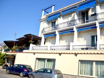 Modernes Hotelgebäude mit blauen Markisen und parkenden Autos davor bei sonnigem Wetter.