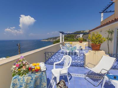 Terrasse mit blauem Boden, weißen Stühlen und Meerblick an einem sonnigen Tag.