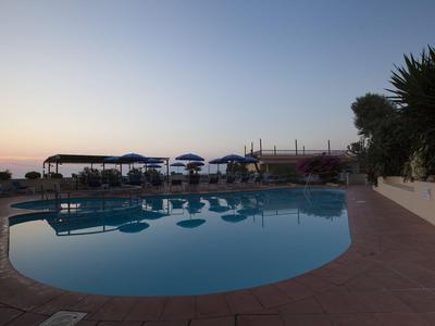 Hotelpool bei Sonnenuntergang mit Sonnenliegen und Blick auf das Meer.