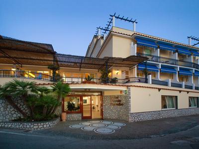 Modernes dreistöckiges Hotel mit Veranda, blauen Dachfenstern und Palmen am Eingang.