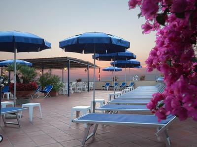 Sonnenliegen und blaue Sonnenschirme auf einer Hotelterrasse mit Blick auf das Meer.
