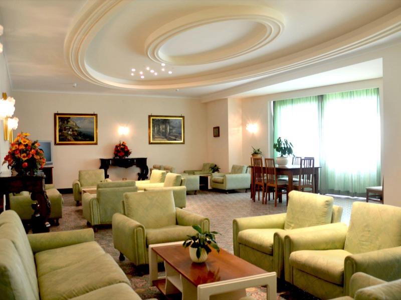 Jasny salon z zielonymi fotelami, kanapami i dużym oknem w tle.