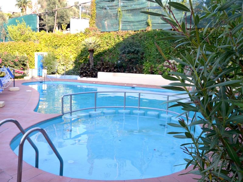 Mały, okrągły basen na zewnątrz hotelu z zielonymi roślinami i leżakami