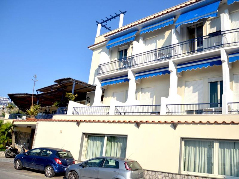 Nowoczesny hotel wielopiętrowy z niebieskimi markizami i zaparkowanymi samochodami przed budynkiem.