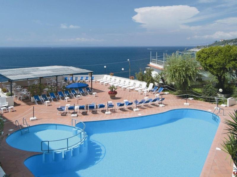 Basen hotelowy z leżakami, parasolami i widokiem na morze w słoneczny dzień