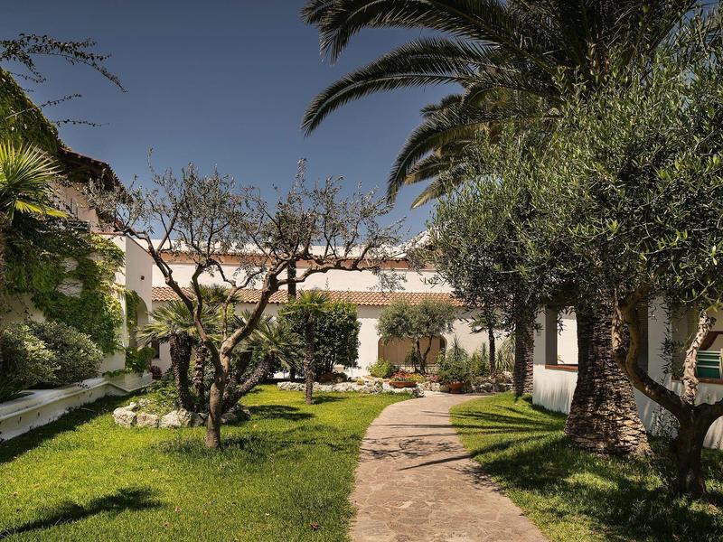 Garden with trees and a path in front of a white building under clear sky.