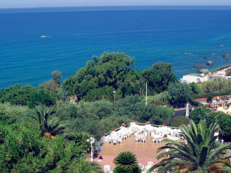 Hotel pool with loungers and palm trees at sunset by the sea