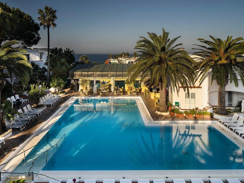Hotel pool with loungers and palm trees at sunset by the sea