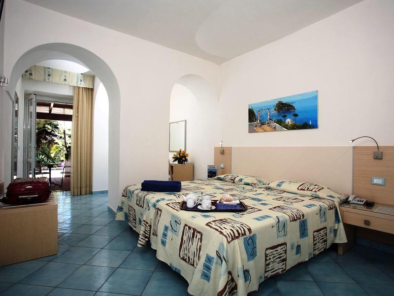 Bedroom with double bed, blue tiled floor, and modern furniture in a bright room.