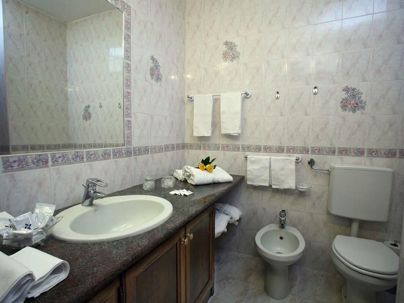 Bright bathroom with sink, bidet, toilet, and towels on the wall.
