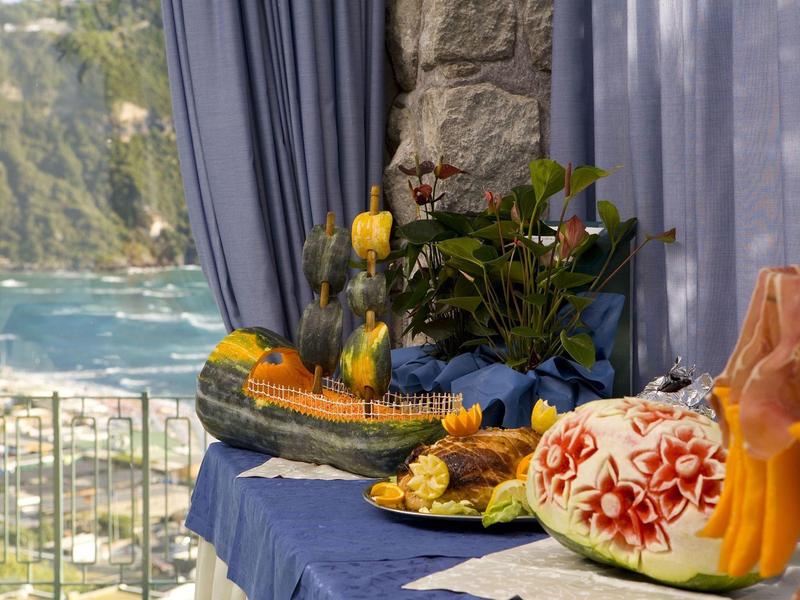 A decorated table with carved vegetables and flowers overlooking the sea and mountains.