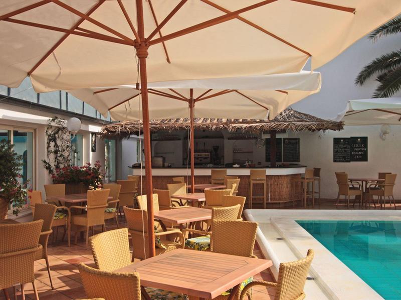 Pool area with umbrellas, tables, and chairs beside a hotel building.