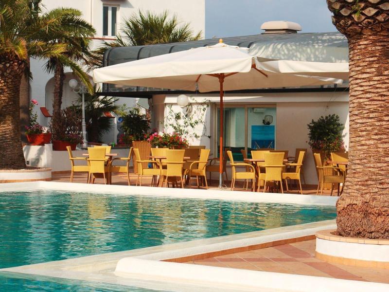 Hotel pool with palm trees and covered seating area under clear sky