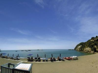 Strand mit Liegestühlen, Sonnenschirmen, sandigem Ufer und blauem Himmel mit wenigen Wolken.