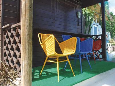 Bunte Stühle auf einem begrünten Balkon neben einer Holzwand.