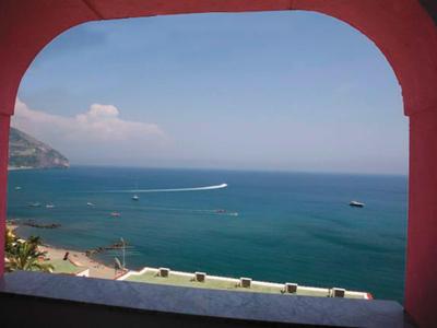 Blick auf das blaue Meer und Boote durch einen bogenförmigen Fensterausschnitt.