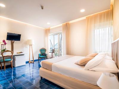 Camera d'hotel luminosa con letto matrimoniale, pavimento blu e finestra con tende.