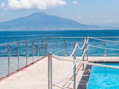 Vista di una piscina sul mare con montagne sullo sfondo in una giornata di sole.