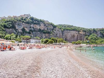 Spiaggia ampia con lettini davanti a alte scogliere e acqua di mare cristallina.