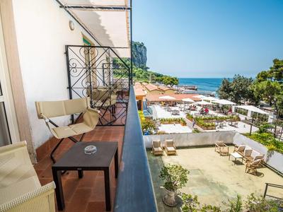 Balcone con sedie e tavolo con vista su piscina e mare con cielo sereno.