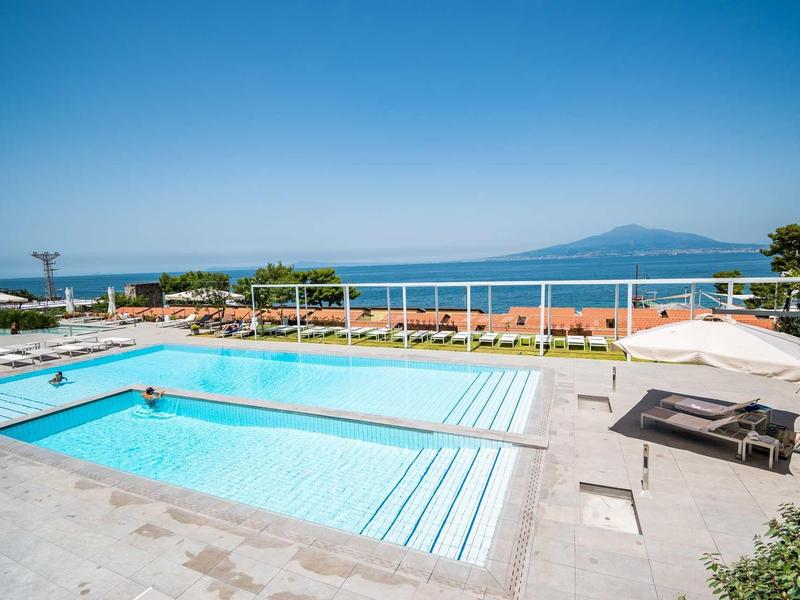 Area piscina moderna con lettini e vista mare sotto un cielo limpido.