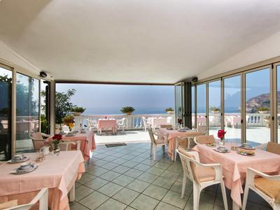 Prosvětlená hotelová jídelna s výhledem na moře a okolní hory.