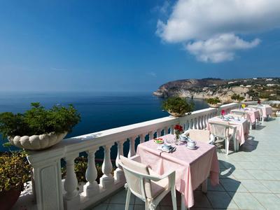 Terrasse mit gedeckten Tischen und pinken Tischdecken, Blick auf Meer und Küstenlandschaft bei klarem Himmel.
