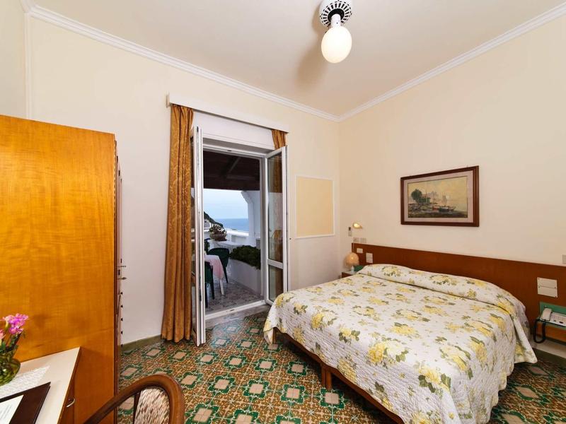 Pohodlný hotelový pokoj s manželskou postelí, přístupem na balkon a barevnou podlahou.