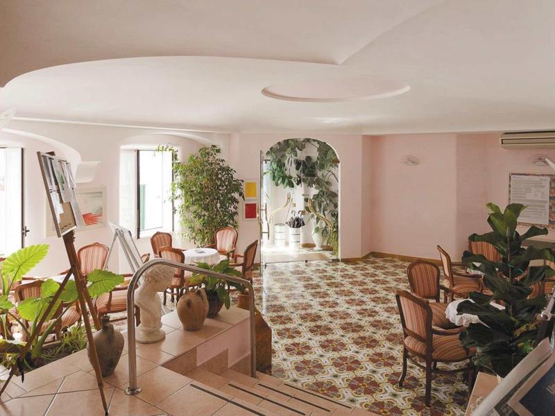 Světlá čekárna s čalouněnými židlemi, rostlinami a vzorovanou podlahou v hotelu.