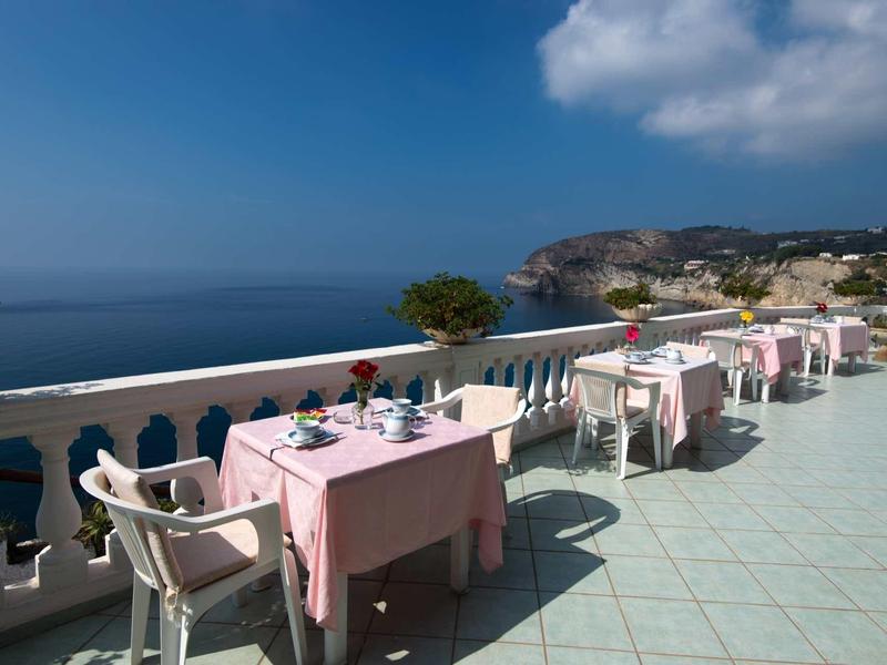 Terasa s prostřenými stoly s výhledem na moře pod jasnou oblohou.