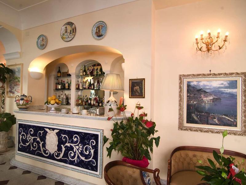 Elegant hotel bar area with classic furniture, plants, and wall decorations.