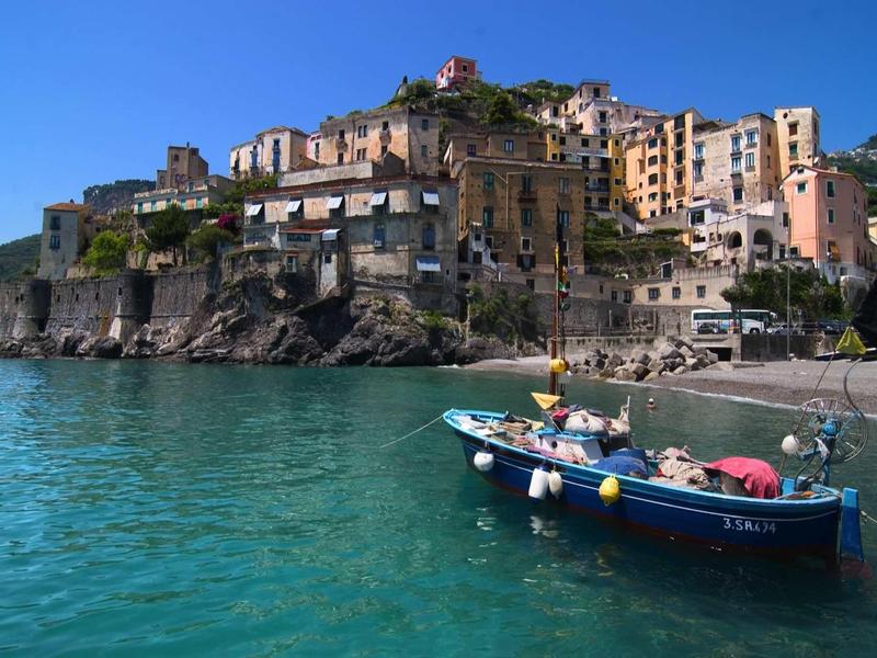 Colorful houses on a cliff over clear blue water with a boat in the foreground.