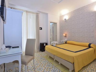 Brightly furnished hotel room with yellow double bed, desk, and wall-mounted flat screen TV.