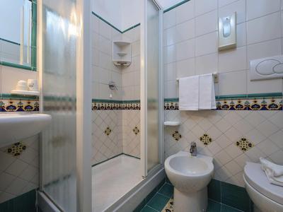 Small bathroom with shower, sink, bidet, and towels.