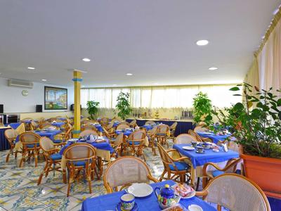 Bright hotel dining room with blue table settings and wooden wicker chairs.