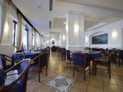 Elegantes Restaurant mit blau gepolsterten Stühlen und großen Fenstern mit weißem Vorhang.