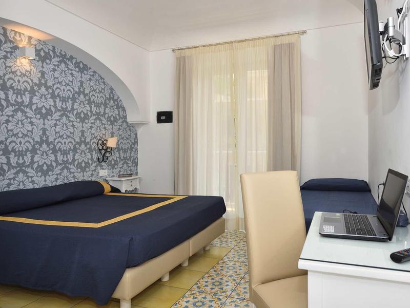 Modern hotel room with double bed, desk, chair, and light curtains.