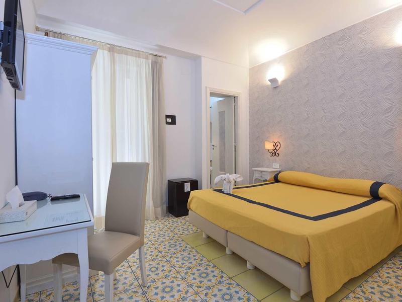 Brightly furnished hotel room with yellow double bed, desk, and wall-mounted flat screen TV.