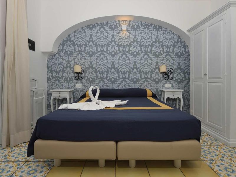 Double room with blue bed, white furniture, and patterned wall in hotel.