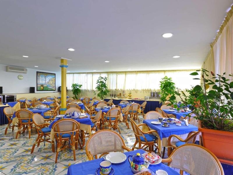 Bright hotel dining room with blue table settings and wooden wicker chairs.