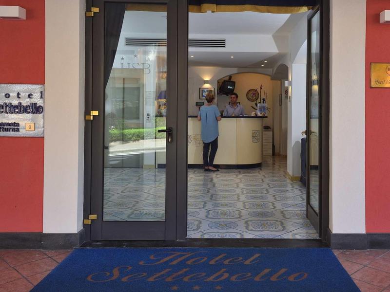 Glass entrance door to a hotel with a blue welcome mat and reception inside.